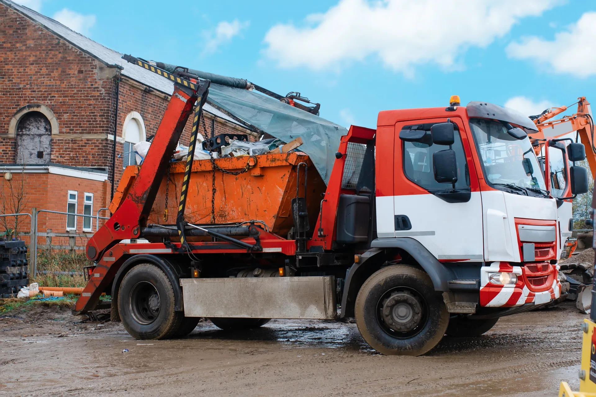 Skip lorry collecting a full builder's skip from a construction site